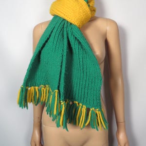 May include: A green and yellow knitted scarf with fringe. The scarf is made of a soft, chunky yarn and has a simple, classic design.