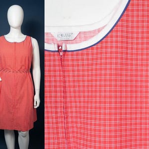 May include: A sleeveless red dress featuring a white grid pattern, a front zipper closure, and a white collar trim with blue piping. The garment includes a waistline with decorative stitching and a side pocket. The interior label reads KOMAR.