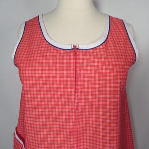May include: Red and white plaid sleeveless dress with a white and blue trim around the neckline and armholes. The dress has a full-length zipper down the front and a pocket with white trim.