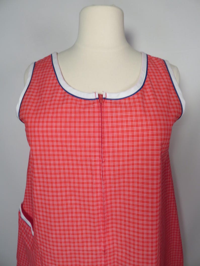 May include: Red and white plaid sleeveless dress with a white and blue trim around the neckline and armholes. The dress has a full-length zipper down the front and a pocket with white trim.