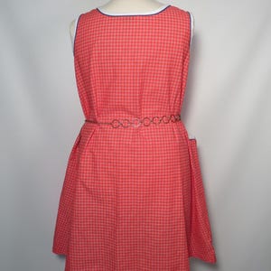 May include: A red and white plaid dress with a white and blue trim neckline. The sleeveless dress has a fitted waist and a flared skirt. A silver chain belt cinches the waist. The dress is displayed on a mannequin.