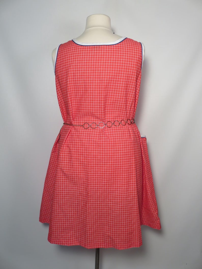 May include: A red and white plaid dress with a white and blue trim neckline. The sleeveless dress has a fitted waist and a flared skirt. A silver chain belt cinches the waist. The dress is displayed on a mannequin.