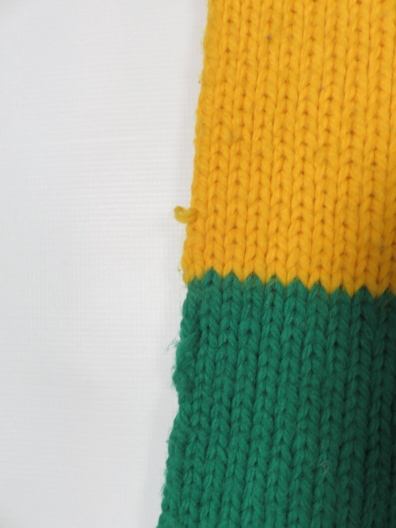 May include: A knitted scarf with yellow and green stripes. The scarf is made of a soft, textured yarn.