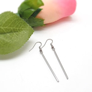 May include: A pair of silver dangle earrings with a long, thin, rectangular bar pendant.