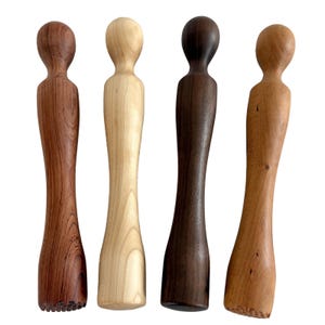 May include: Four wooden muddlers arranged in a vertical row, each featuring a rounded top handle and a cylindrical body. The muddlers display distinct wood grain patterns and colors, ranging from light beige to medium brown and dark espresso brown.