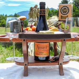 May include: A wooden wine and cheese serving table with two wine glasses, a bottle of Amavi Syrah wine, a jar of Divina Sour Cherry Spread, a box of 349 Crisps Whole Grain crackers, and a cheese board with cheese and cherries.