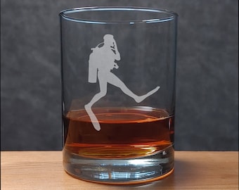 May include: A clear glass tumbler with a silhouette of a scuba diver etched on the side. The glass is filled with amber-coloured liquid.