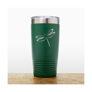 May include: A green stainless steel tumbler with a dragonfly design engraved on the side. The tumbler has a lid and is insulated to keep drinks cold or hot.
