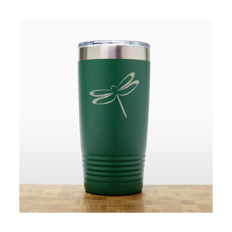 May include: A green stainless steel tumbler with a dragonfly design engraved on the side. The tumbler has a lid and is insulated to keep drinks cold or hot.