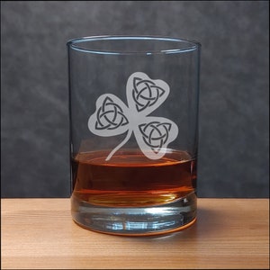 May include: A clear glass tumbler with a Celtic knot shamrock design etched on the front. The glass is filled with amber liquid.