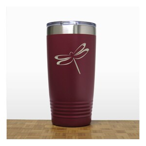 May include: A maroon stainless steel tumbler with a dragonfly design engraved on the side. The tumbler has a silver lid and a textured bottom.
