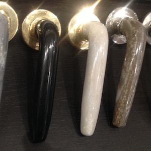 Può includere: Cinque maniglie per porte in diverse finiture. Le maniglie sono tutte in metallo e hanno una forma curva. Le finiture includono grigio, nero, bianco, marrone e grigio chiaro.