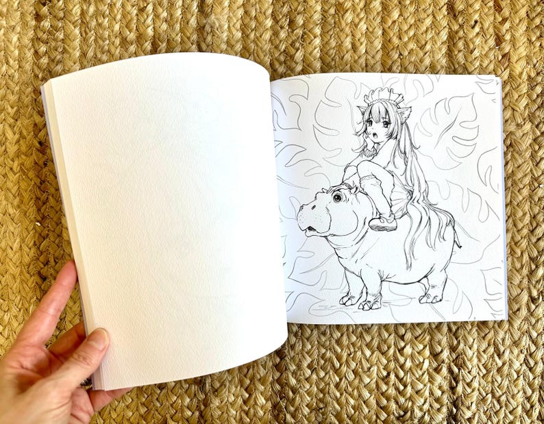 以下が含まれることがあります： 白紙のページと、カバに乗るキャラクターの白黒イラストが描かれた、開いた塗り絵。イラストは葉の模様で囲まれています。本は手で開かれています。
