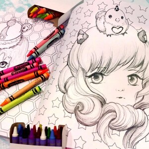 May include: An open coloring book with two black and white illustrations of anime-style girls. One girl is wearing a crown and the other is wearing a unicorn on her head. The book is surrounded by a variety of crayons.