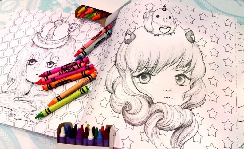 May include: An open coloring book with two black and white illustrations of anime-style girls. One girl is wearing a crown and the other is wearing a unicorn on her head. The book is surrounded by a variety of crayons.