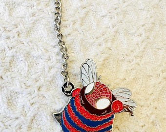 May include: A metal lapel pin featuring a bee with a red and blue striped body and a red webbed pattern on its head. The bee has white wings and is attached to a silver-toned metal chain and a pin backing with a secure clutch mechanism.