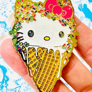 May include: Gold-colored enamel pin featuring Hello Kitty as an ice cream cone with colorful sprinkles and a pink bow.