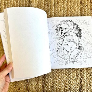 以下が含まれることがあります： 開いた塗り絵。女の子がライオンを頭に乗せて眠っている白黒イラスト。ページは空白で、塗り絵の準備ができています。背景には足跡があります。