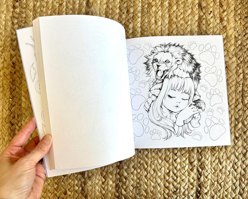 以下が含まれることがあります： 開いた塗り絵。女の子がライオンを頭に乗せて眠っている白黒イラスト。ページは空白で、塗り絵の準備ができています。背景には足跡があります。