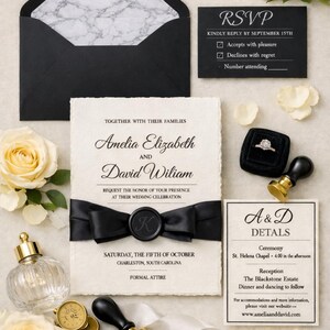 May include: A wedding invitation suite featuring a cream-colored card with deckled edges, black text, and a black ribbon with a wax seal. Includes a black envelope with marble lining, an RSVP card, a details card, a ring in a box, and a wax stamp.