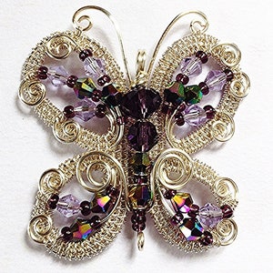 May include: A handcrafted butterfly pendant made of gold-colored wire, adorned with purple and iridescent beads. The wings feature intricate wirework and are embellished with various sizes of faceted beads. The butterfly's body is a cluster of purple beads.