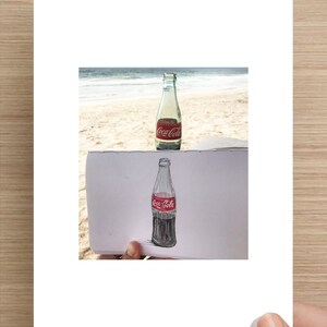 May include: A drawing of a Coca-Cola bottle on a piece of paper, with a real Coca-Cola bottle in the background.