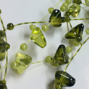 May include: A strand of green glass beads with a triangular shape. The beads are strung on a clear wire.