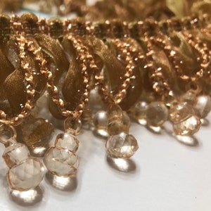 May include: Gold trim with a chain and clear glass beads hanging from it. The beads are faceted and have a teardrop shape.