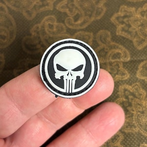 Könnte beinhalten: Ein schwarzer und weißer gestickter Aufnäher mit einem weißen Totenkopf- und Knochen-Motiv. Der Aufnäher ist rund und hat einen schwarzen Rand.