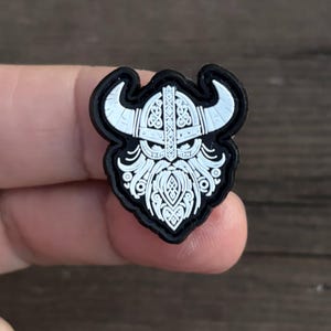 May include: A black and white rubber patch with a detailed design of a Viking warrior's head wearing a horned helmet.