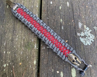 May include: A gray and red paracord bracelet with a metal clasp and a metal skull charm.