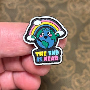 May include: A black and white cartoon earth with a rainbow and clouds above it. The earth has a smiling face with pink cheeks. The text "THE END IS NEAR" is written below the earth.