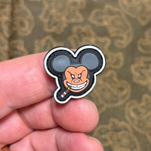 May include: A black and white embroidered patch featuring a cartoon image of Mickey Mouse with a menacing expression and a cigarette in his mouth. The patch has a white border.