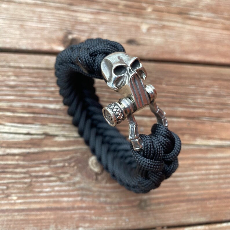 May include: Black paracord bracelet with a silver skull clasp. The clasp has a detailed skull design and a small silver button.