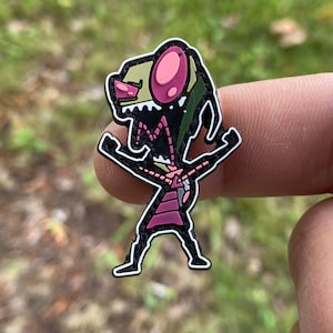May include: A black and green cartoon character with pink eyes and a wide open mouth. The character is standing with its arms raised in the air. The character is a pin.