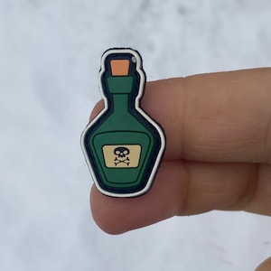 May include: A green glass bottle with a skull and crossbones label. The bottle has a white outline and a cork stopper.