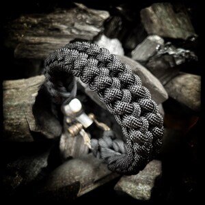 May include: A black paracord bracelet with a braided design. The bracelet is made of durable nylon cord and is designed to be strong and long-lasting.
