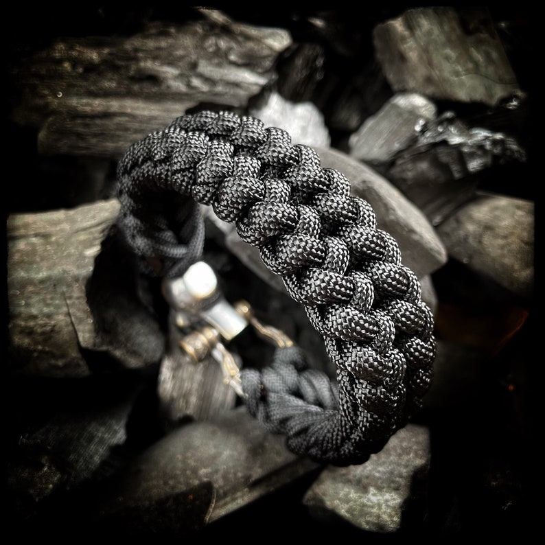 May include: A black paracord bracelet with a braided design. The bracelet is made of durable nylon cord and is designed to be strong and long-lasting.