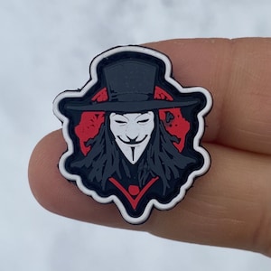 Könnte beinhalten: Ein schwarz-weißes Patch mit einem stilisierten Bild von V wie Vendetta, der einen Zylinder und eine Maske trägt. Das Patch hat einen roten und weißen Hintergrund.