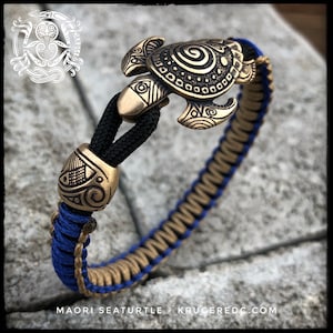 Peut inclure: Un bracelet en paracorde bleu et or avec un pendentif en bronze représentant une tortue de mer maorie. Le pendentif présente des sculptures complexes et un motif en spirale. Le bracelet est réglable et possède un fermoir sécurisé.