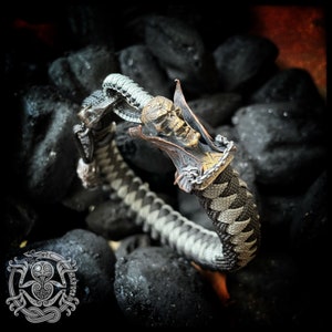 May include: A black and white paracord bracelet with a skull-shaped metal clasp. The clasp is made of copper and has a detailed design.