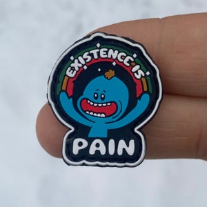 May include: A black and white shoe charm featuring a cartoon character. The charm has a blue figure with a large red mouth and the words "EXISTENCE IS" above and "PAIN" below. A rainbow arc surrounds the character.