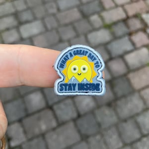 May include: A grey and blue patch with a smiling yellow sun and the text "What a great day to stay inside".