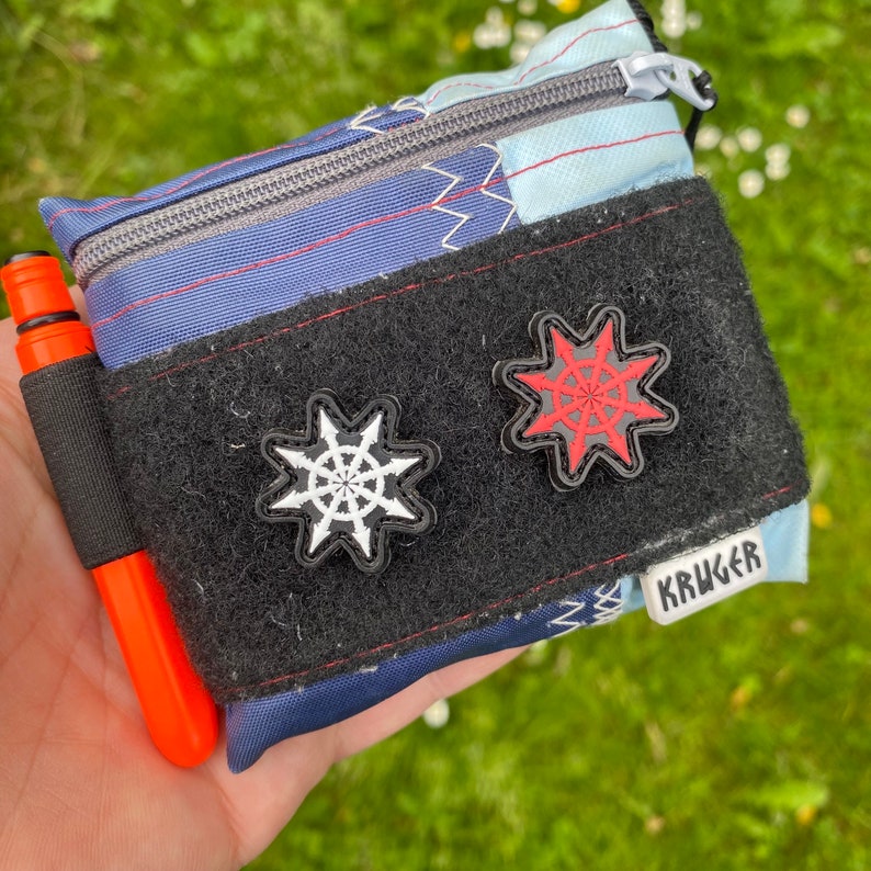 Puede incluir: Una bolsa de tela azul y blanca con una correa negra y dos parches en forma de estrella en blanco y negro. La bolsa tiene una cremallera y el texto "KRUGER" est&aacute; impreso en la parte delantera.
