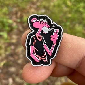 May include: Pink Panther cartoon character wearing sunglasses and a black shirt, holding a phone with a white background. The character is outlined in black and white.