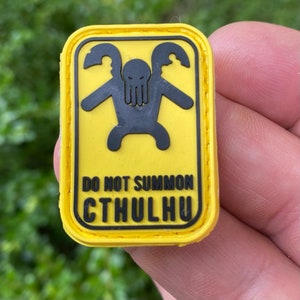 May include: Yellow patch with black stitching and a black graphic of a tentacled creature with the text "Do Not Summon Cthulhu".