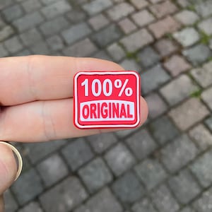 Può includere: Toppa rettangolare rossa con testo bianco che recita "100% ORIGINALE".
