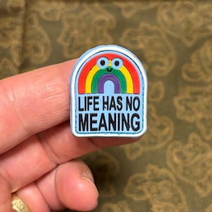 Könnte beinhalten: Ein blauer und weißer Gummianhänger mit einem Regenbogen und dem Text "LIFE HAS NO MEANING".