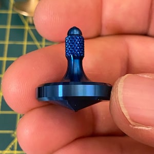 Op de afbeelding: Een blauwe metalen draaitop met een getextureerde bovenkant en een puntige onderkant.
