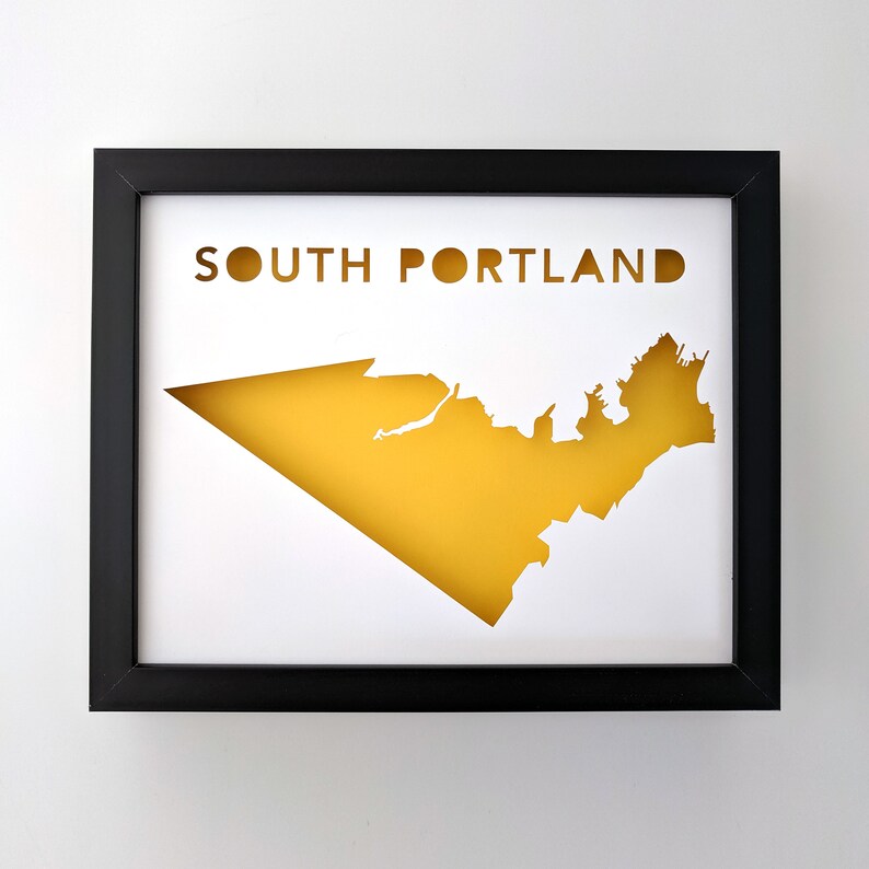 Peut inclure: Une impression encadr&eacute;e noire avec un fond blanc et une silhouette jaune des limites de la ville de South Portland, Maine. Le texte "SOUTH PORTLAND" est imprim&eacute; en noir en haut de l'impression.